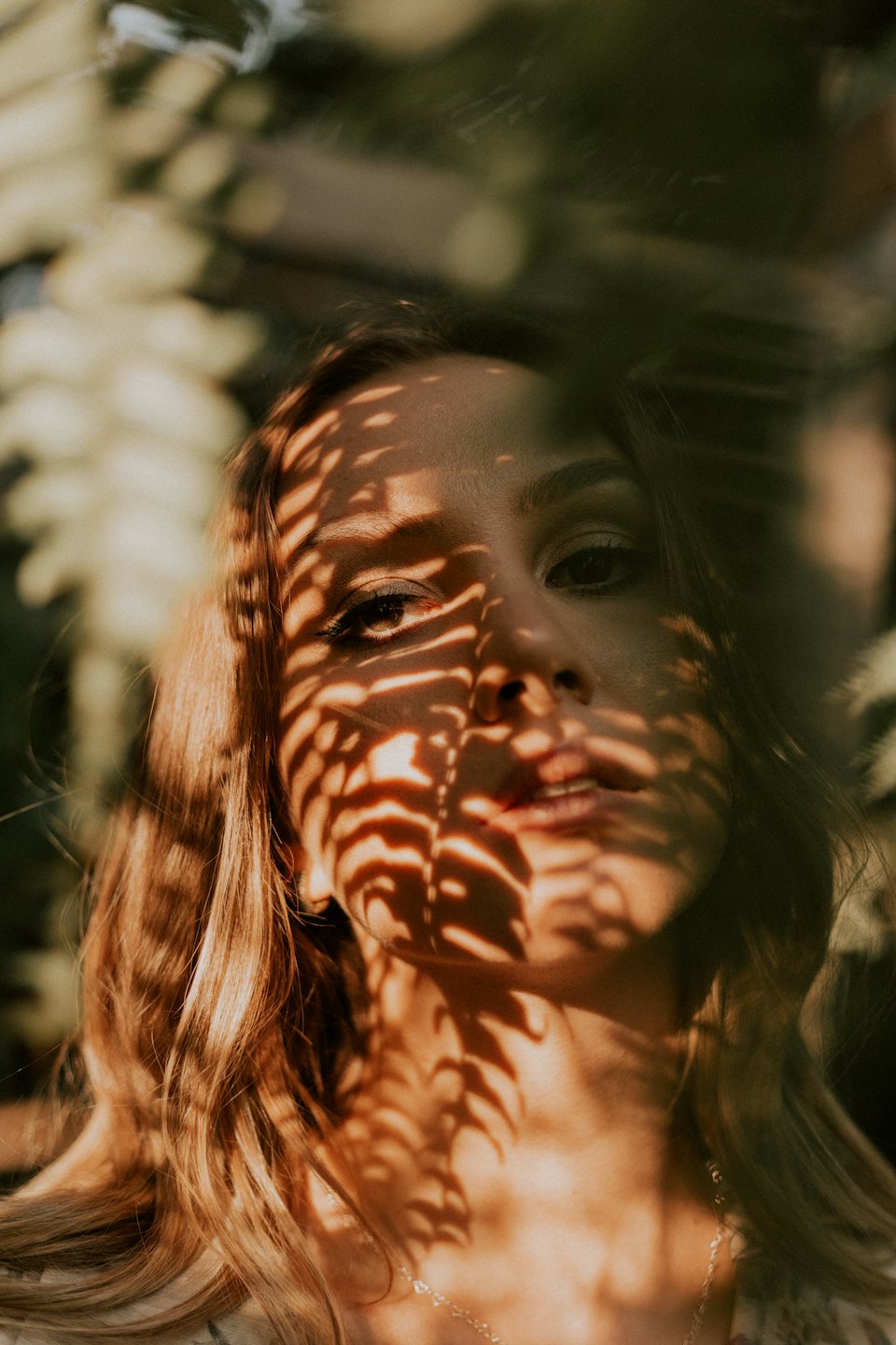 Young woman with leaf shadows on her face outdoors.